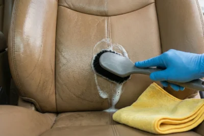 Primer plano de limpieza de asiento de cuero, mostrando la diferencia entre la parte sucia y brillante y la parte limpia con acabado mate natural.